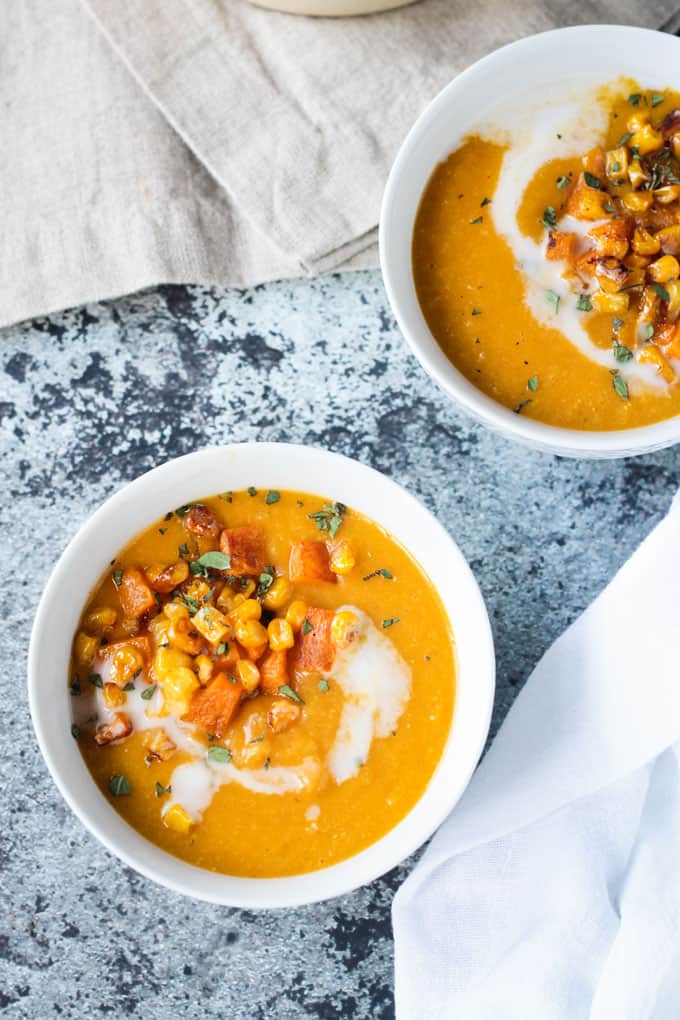 Two bowls of vegan butternut squash soup with corn on a slate tabletop with a beige napkin.
