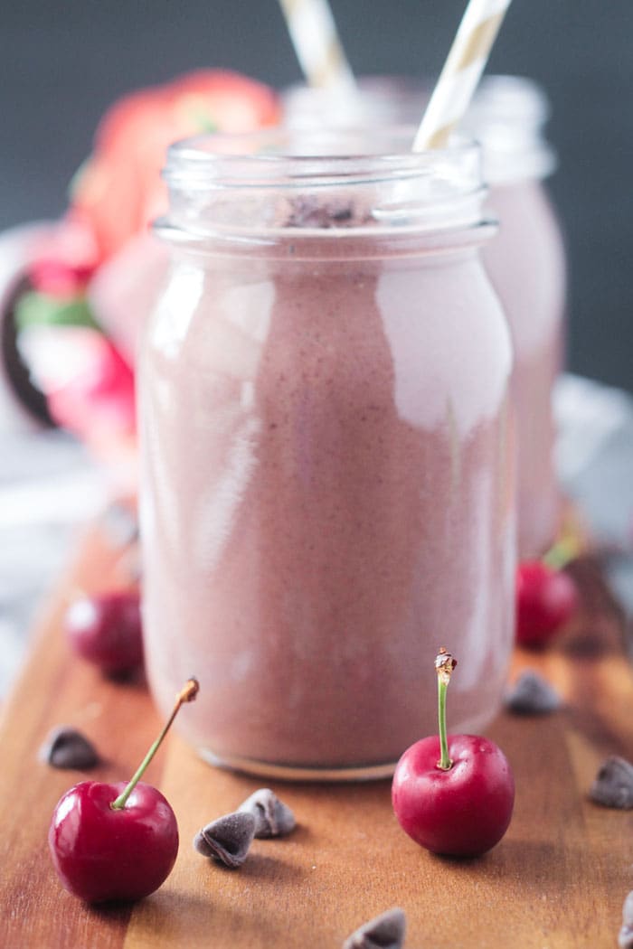 Two deep red fresh cherries on a wooden board in front of two glass jars