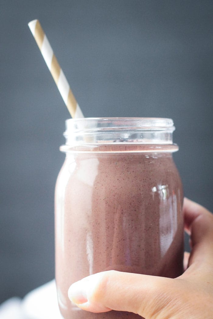 Hand holding a glass of chocolate covered cherry smoothie with a gold and whites striped straw.