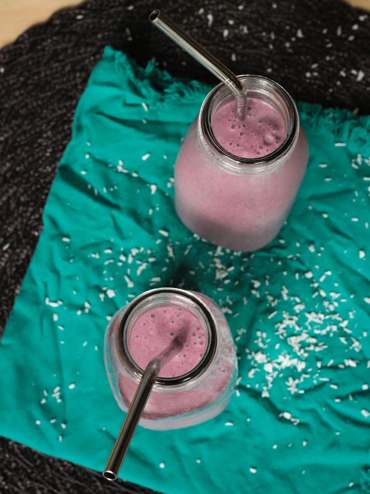 Two Coconut Berry Smoothies in glasses on a green dish cloth. Metal straws in both glasses.