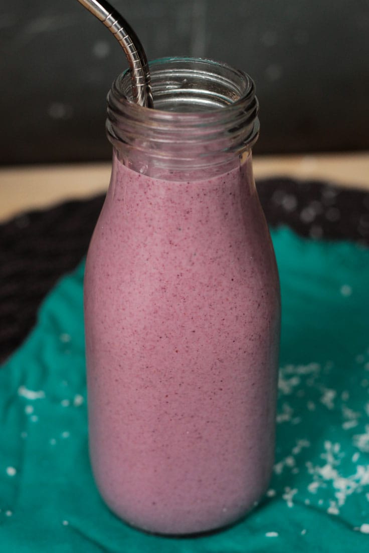 Coconut Berry Smoothie in a tall skinny glass with a metal straw. Shredded coconut scattered around the glass.