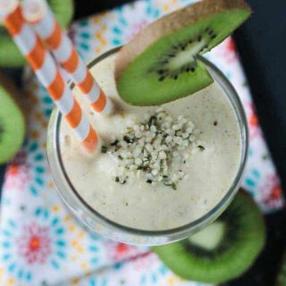 overhead view of a smoothie with two orange and white striped straws and a slice of kiwi on the side of the glass