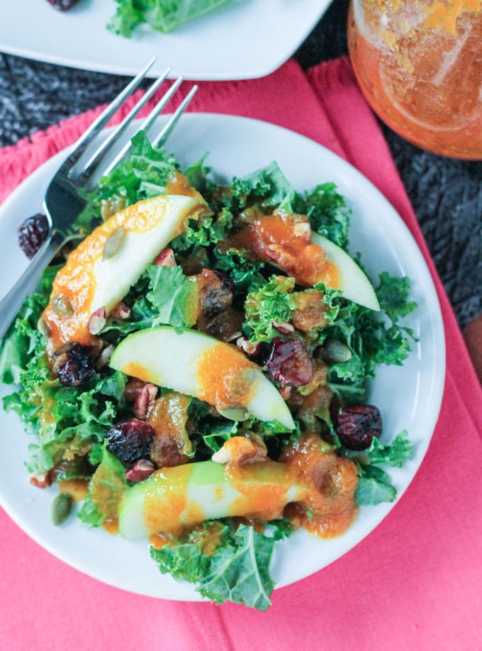 Autumn Kale Apple Salad w/ Warm Pumpkin Vinaigrette - protein packed, sweet and tart, and highly nutritious. The perfect light fall lunch or a starter for a heartier meal. Overhead view of a plate of Autumn Kale Apple Salad with Warm Pumpkin Vinaigrette. A silver fork lies on the side of the plate.