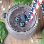 Overhead view of a blueberry oatmeal smoothie in a glass jar topped with three fresh blueberries.