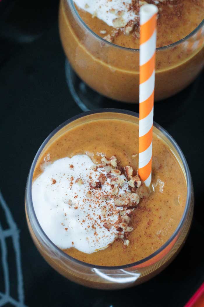 Overhead view of a Pumpkin Pie Smoothie topped with dairy free whipped cream and chopped pecans.