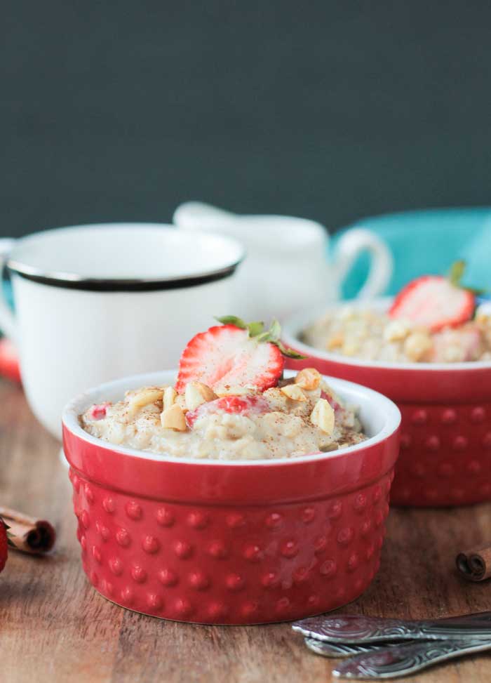 Creamy oatmeal in a red bowl with a coffee cup behind