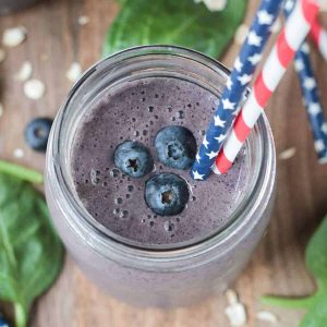 three fresh blueberries and two straws in a glass of blueberry smoothie
