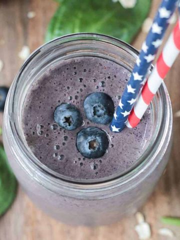 three fresh blueberries and two straws in a glass of blueberry smoothie