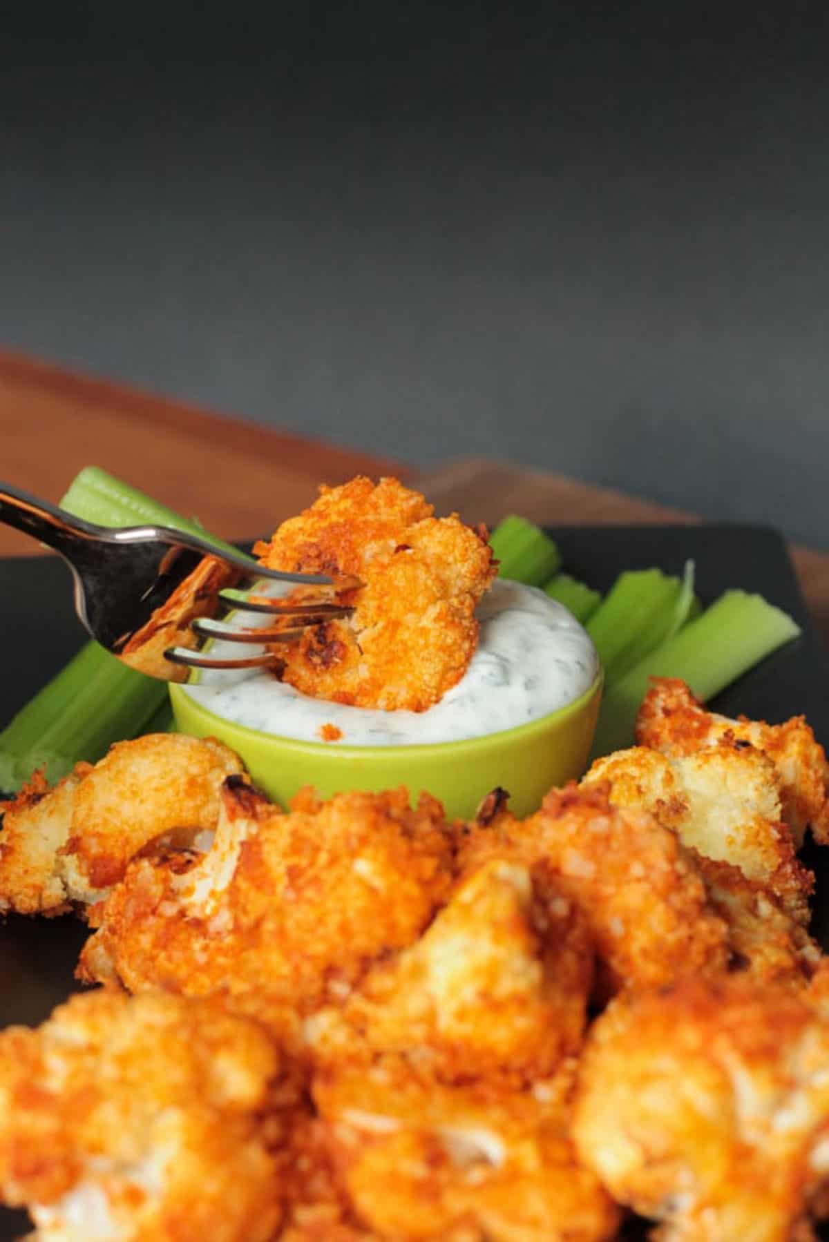 Cauliflower floret on a fork being dipped into ranch.