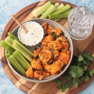 Plate of vegan buffalo cauliflower bites on a plate with celery sticks and small bowl of ranch.