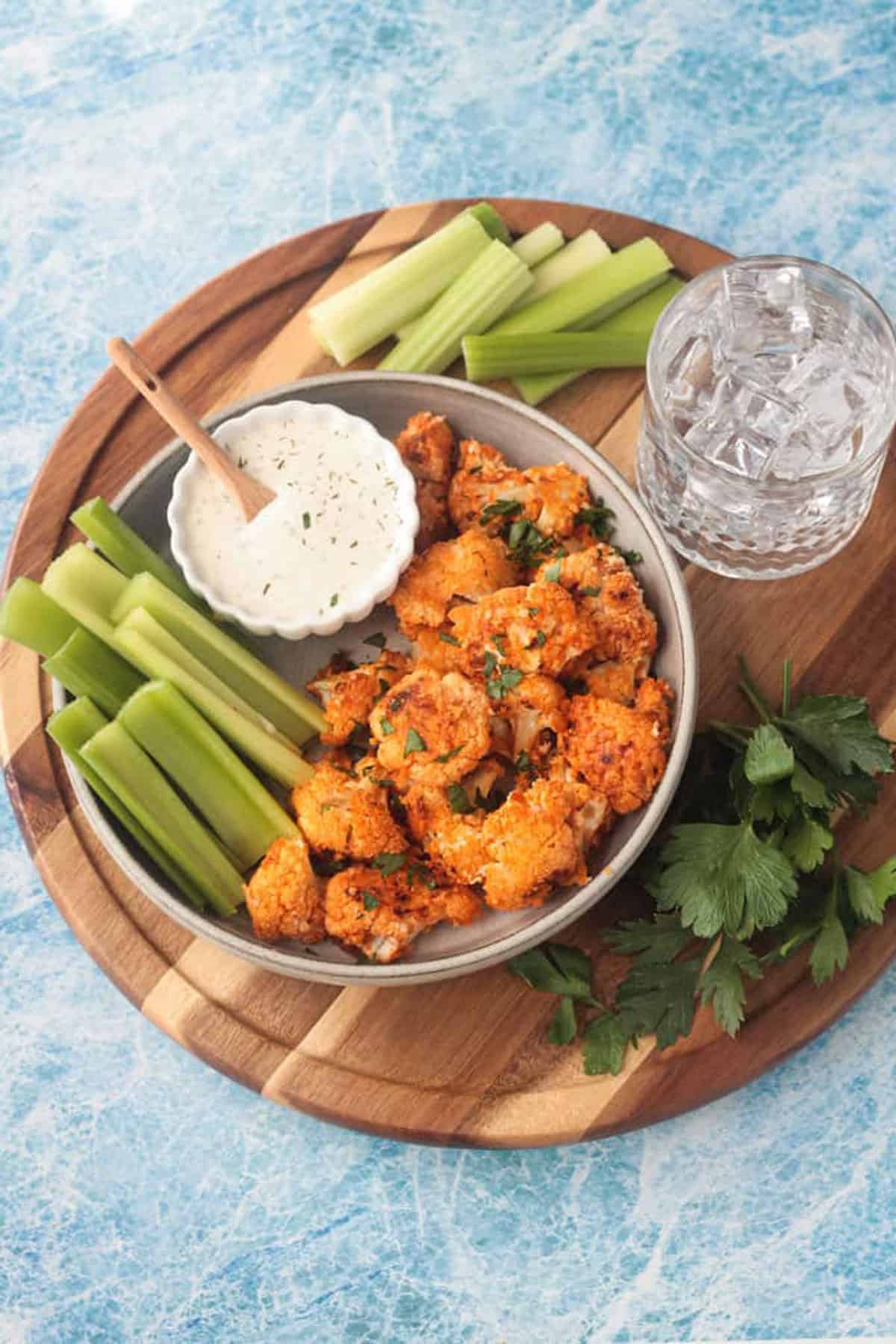Plate of vegan buffalo cauliflower bites on a plate with celery sticks and small bowl of ranch.