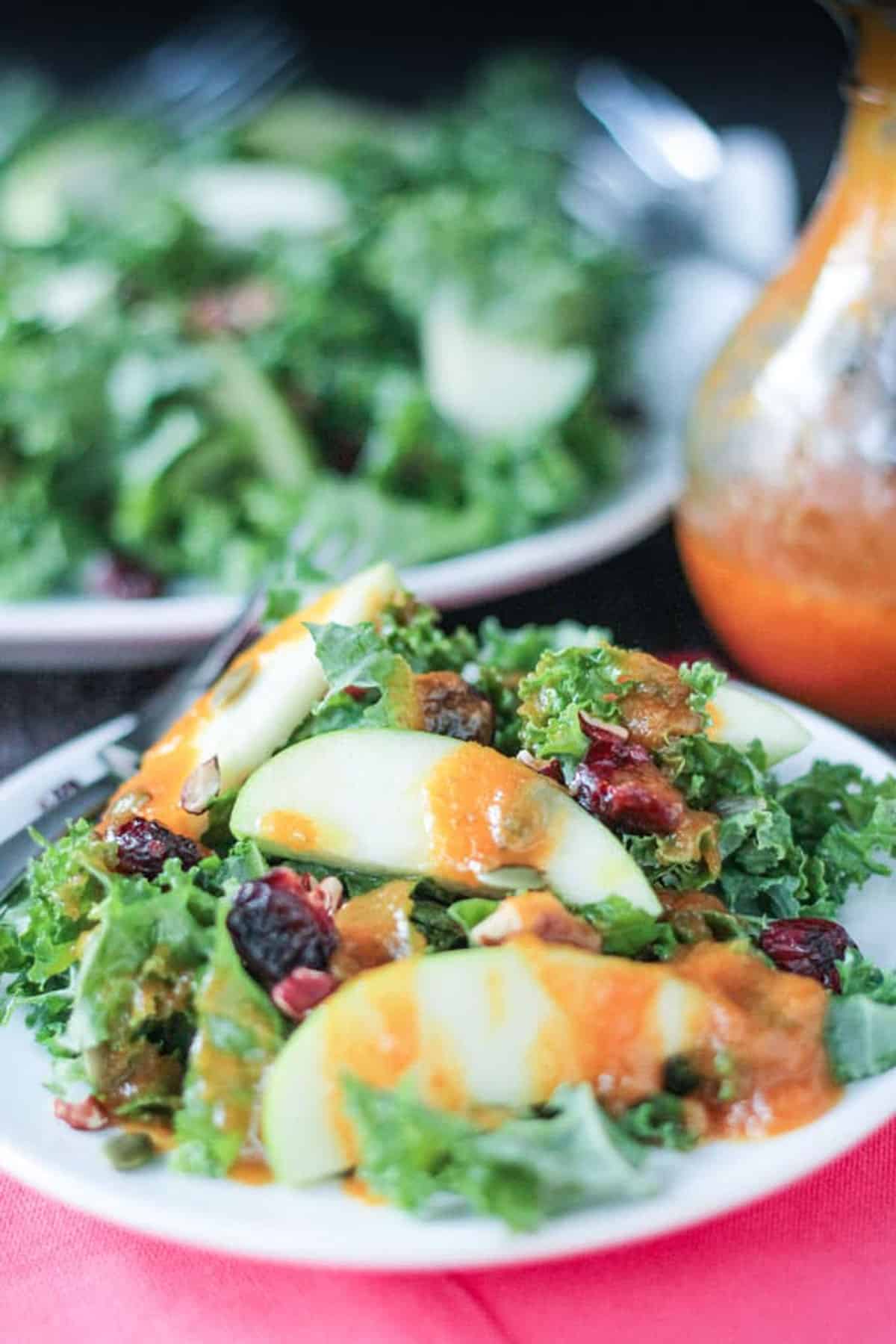 Autumn Kale Apple Salad w/ Warm Pumpkin Vinaigrette - protein packed, sweet and tart, and highly nutritious. The perfect light fall lunch or a starter for a heartier meal. Close up of pumpkin dressing drizzled over a salad.