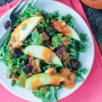 Overhead view of a kale salad with apples, dried cranberries, nuts and seeds.