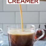 Pumpkin spice creamer being poured from a bottle into a cup of coffee.