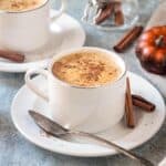 Cup of pumpkin spice coffee on a saucer with a spoon and two cinnamon sticks.