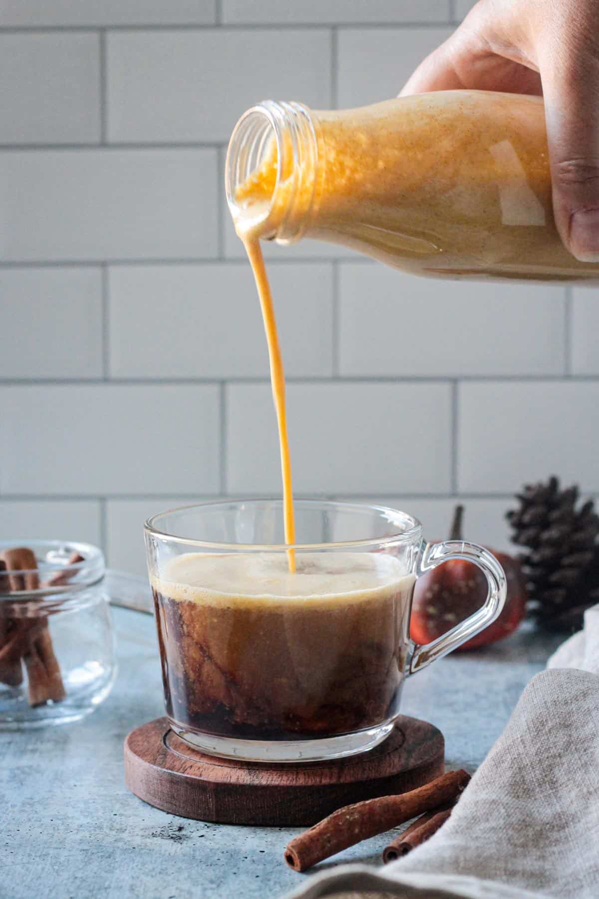 Pumpkin spice creamer being poured into a glass coffee cup.