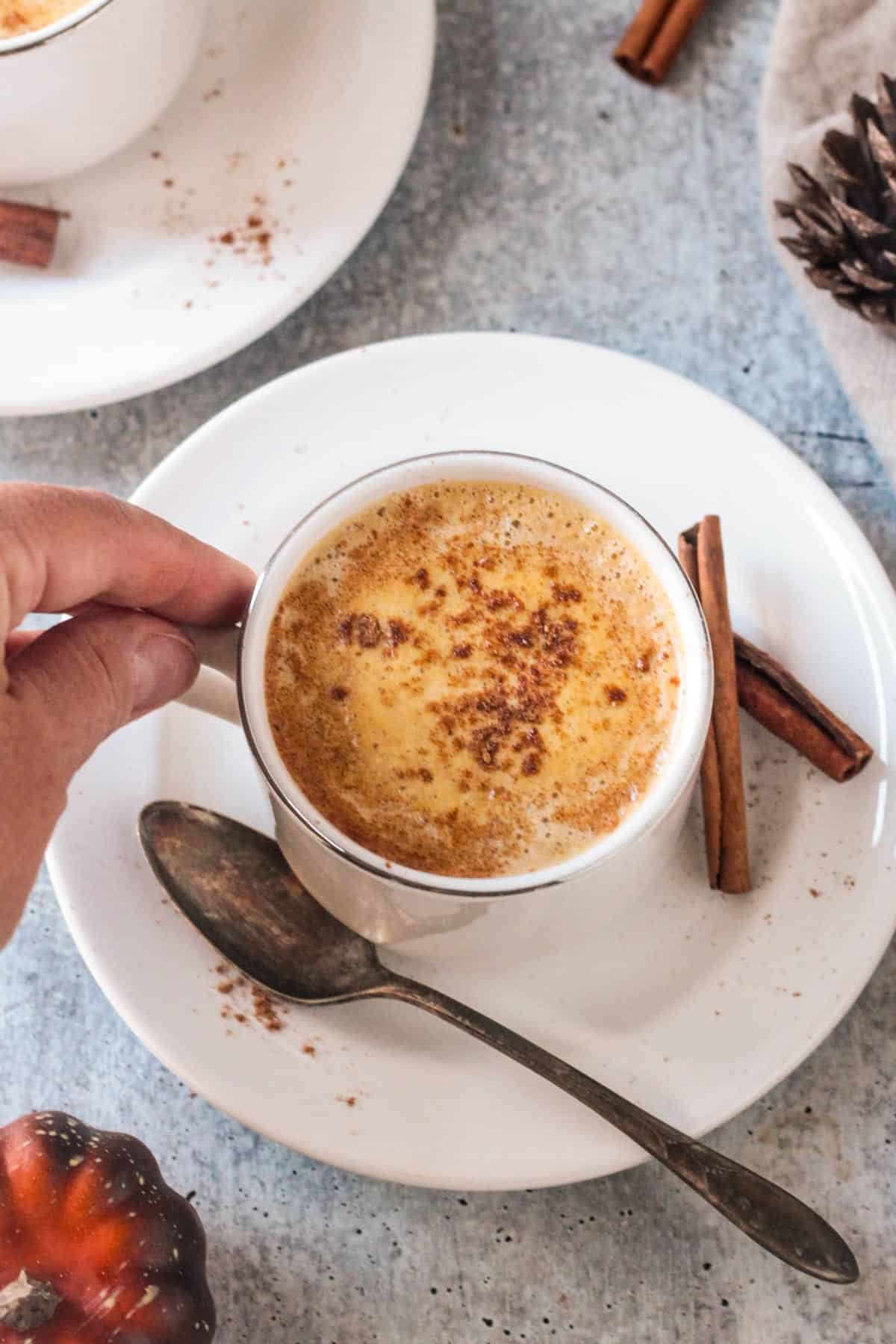 Hand grabbing the handle of a cup of coffee.