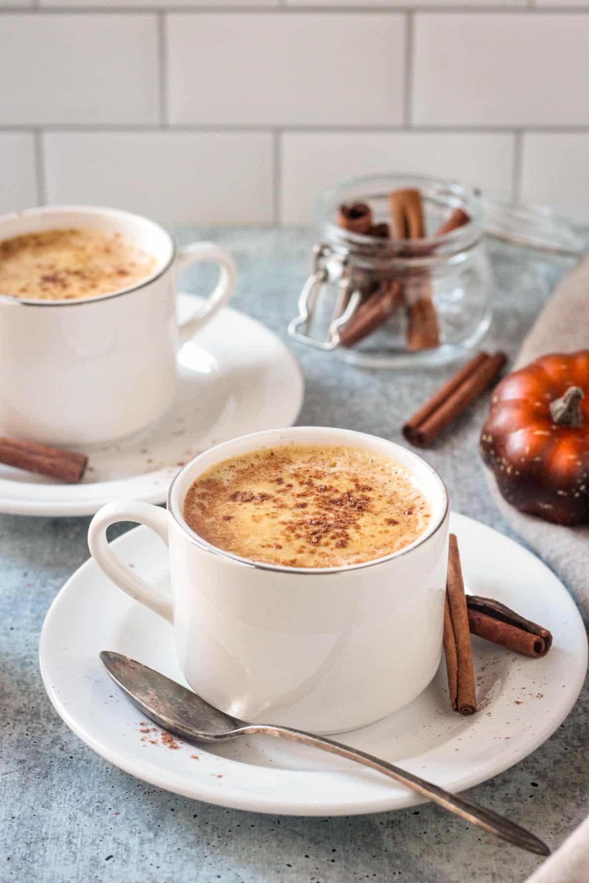 Cup of pumpkin spice coffee on a saucer with a spoon and two cinnamon sticks.