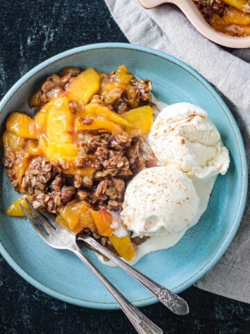 Vegan peach crisp with two scoops of vanilla ice cream on a blue plate.