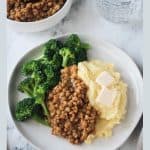 BBQ lentils with mashed potatoes and steamed broccoli on a white plate.