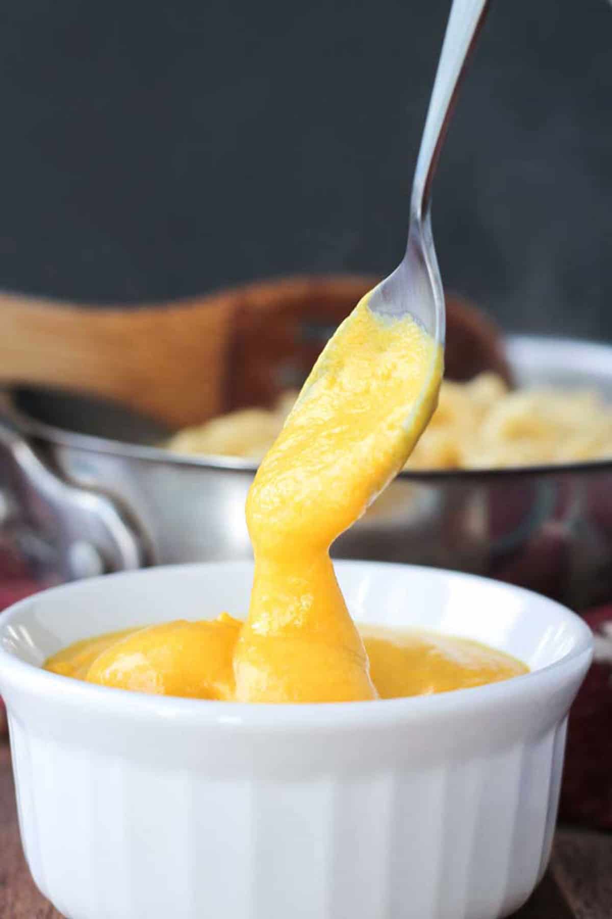 Spoonful of butternut squash mac and cheese sauce being poured into a bowl.