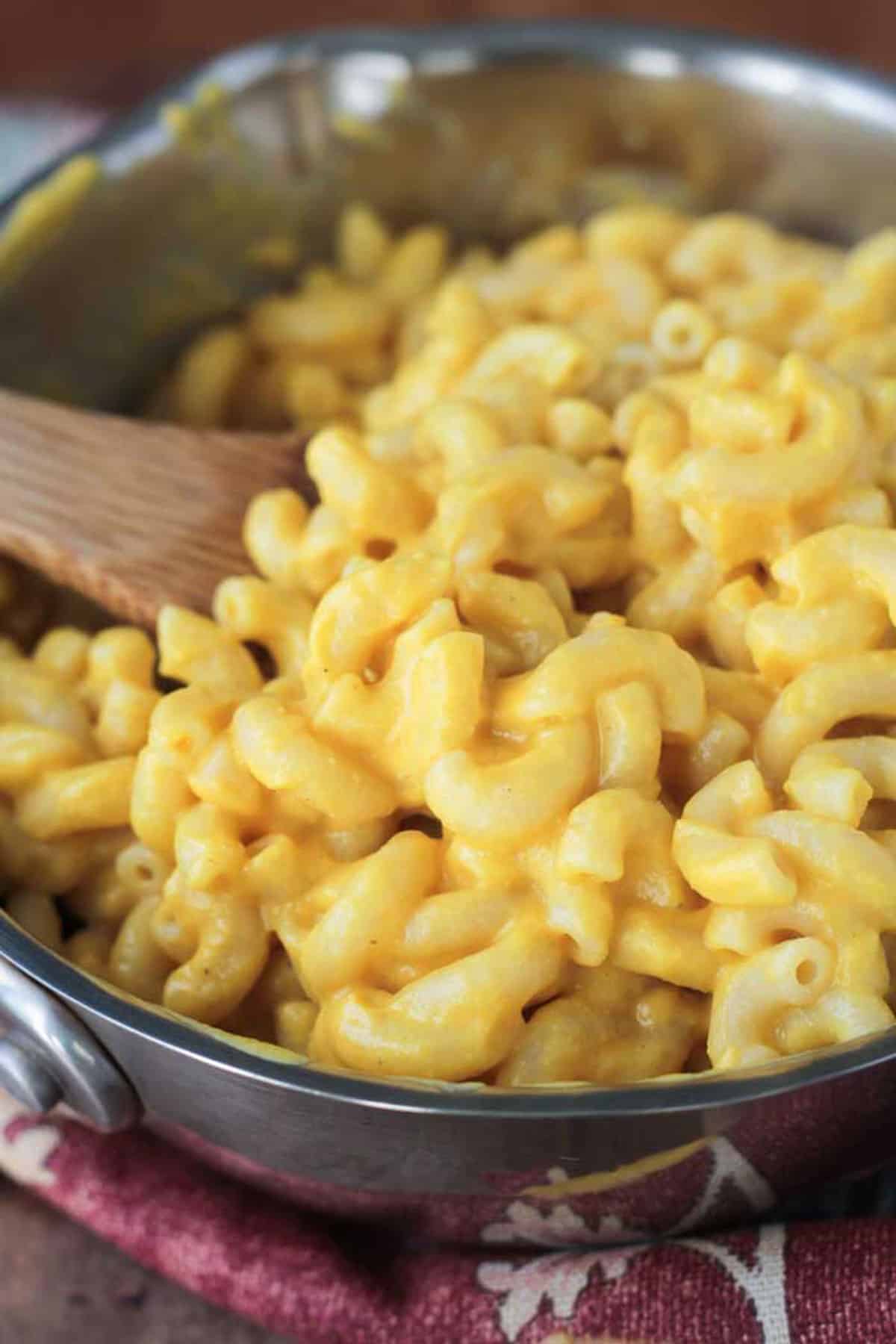 Wooden spoon stirring a skillet of vegan mac and cheese.