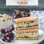 Stacked vegan chickpea salad sandwich halves on a plate with a bunch of red grapes.