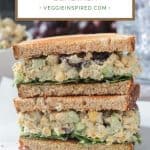 Stacked vegan chickpea salad sandwich halves on a plate with a bunch of red grapes.
