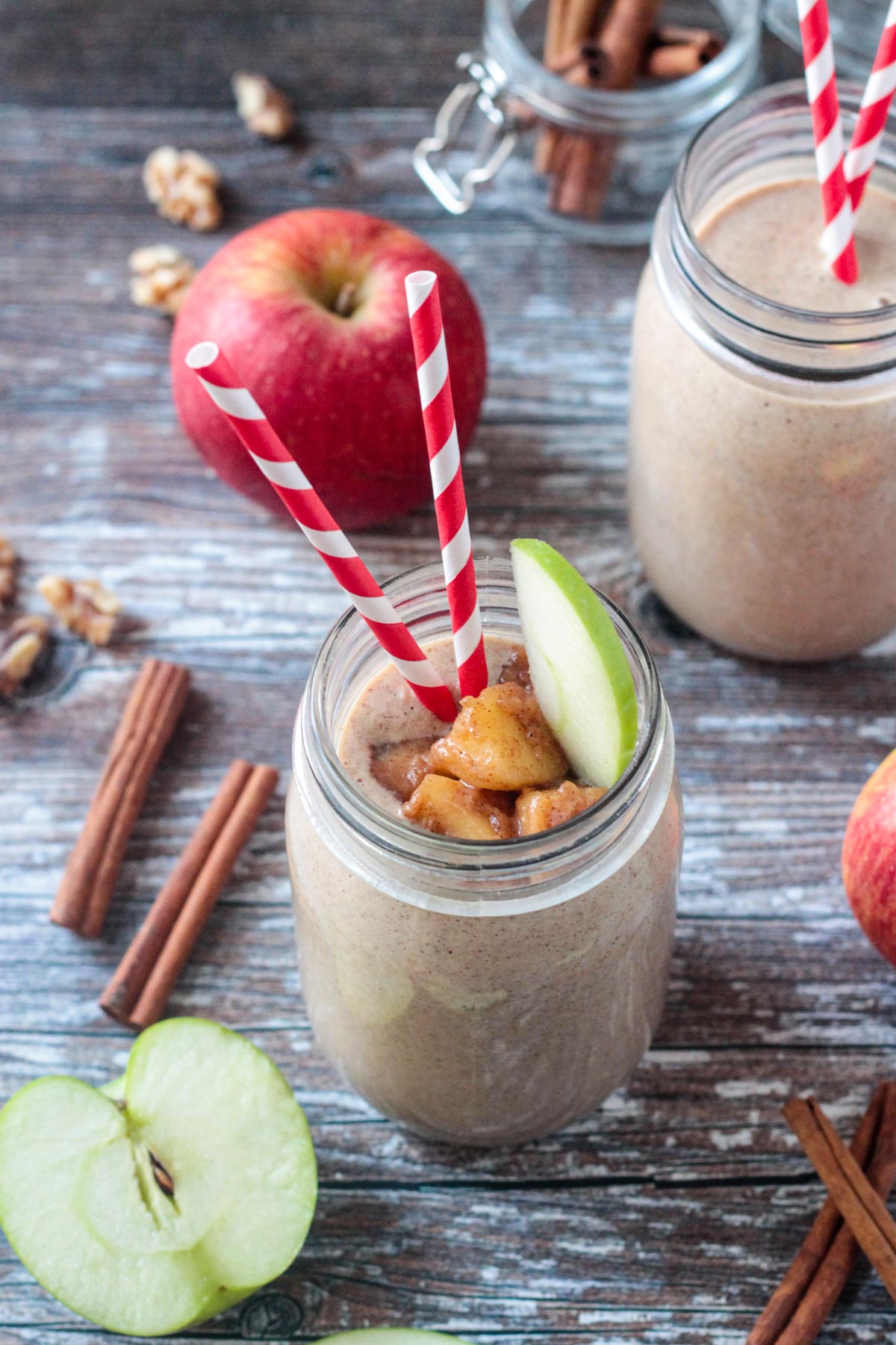 Two smoothies surrounded by apples and cinnamon sticks.
