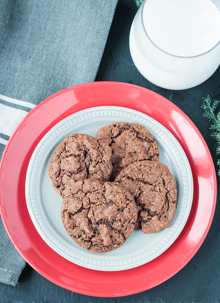 Small gray plate of 5 Chocolate Almond Cookies on a larger red plate. Glass of milk behind.
