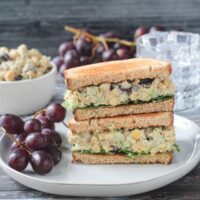 Stacked vegan chickpea salad sandwich halves on a plate with a bunch of red grapes.