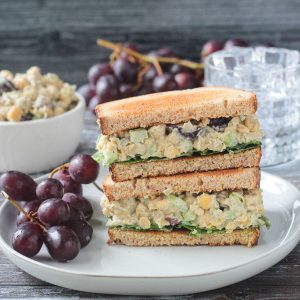 stablet vegansk kikert salat sandwich halvdeler på en plate med en haug med røde druer.