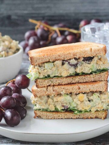 Stacked vegan chickpea salad sandwich halves on a plate with a bunch of red grapes.