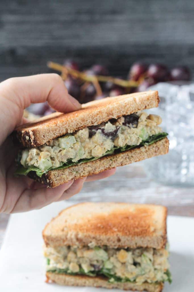Hand holding up a half of a vegan chickpea salad sandwich.
