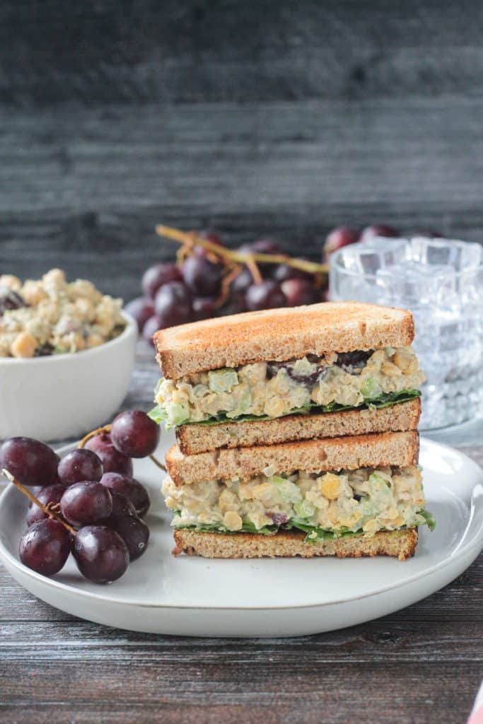 Stacked sandwich halves on a plate with a bunch of red grapes.