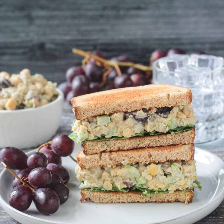 Stacked sandwich halves on a plate with a bunch of red grapes.