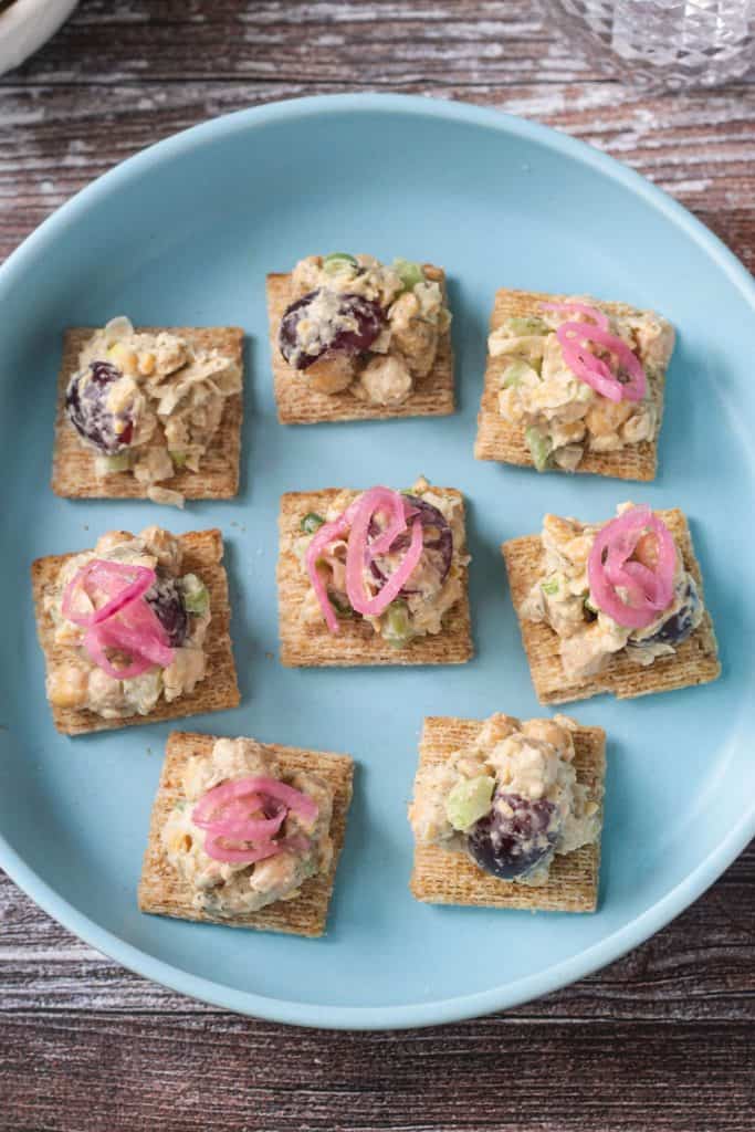 8 wheat crackers topped with chickpea salad and pickled red onions on a blue plate.