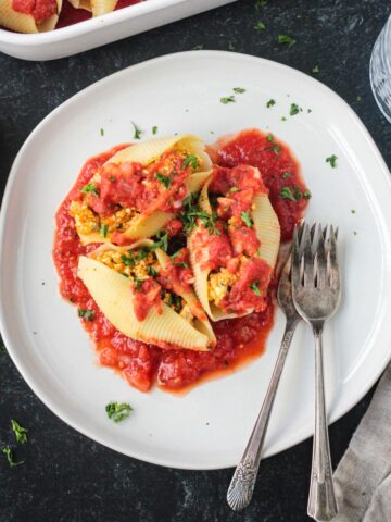 Three vegan stuffed shells on a plate over extra sauce.