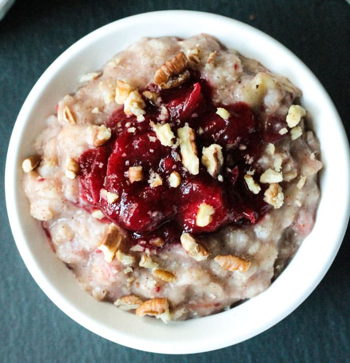 Close up overhead view of a bowl of creamy oatmeal topped with cranberry sauce and pecans.