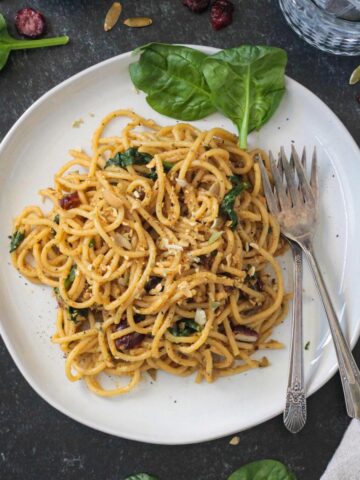 Spaghetti with spinach and cranberries on a plate with two forks.