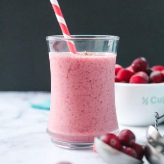Vibrant red speckled cranberry smoothie in a glass with a red and white straw.