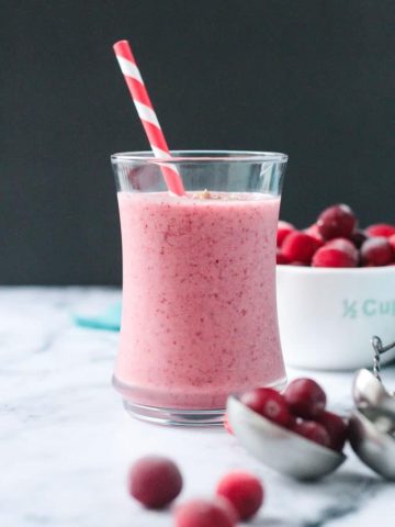 Vibrant red speckled cranberry smoothie in a glass with a red and white straw.