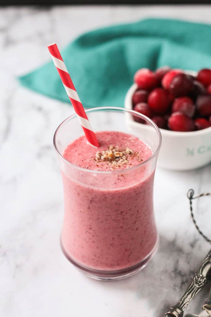 Cranberry smoothie in front of a bowl of fresh cranberries and an aqua blue napkin.
