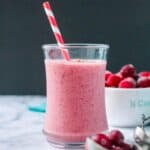 Vibrant red speckled cranberry smoothie in a glass with a red and white straw.