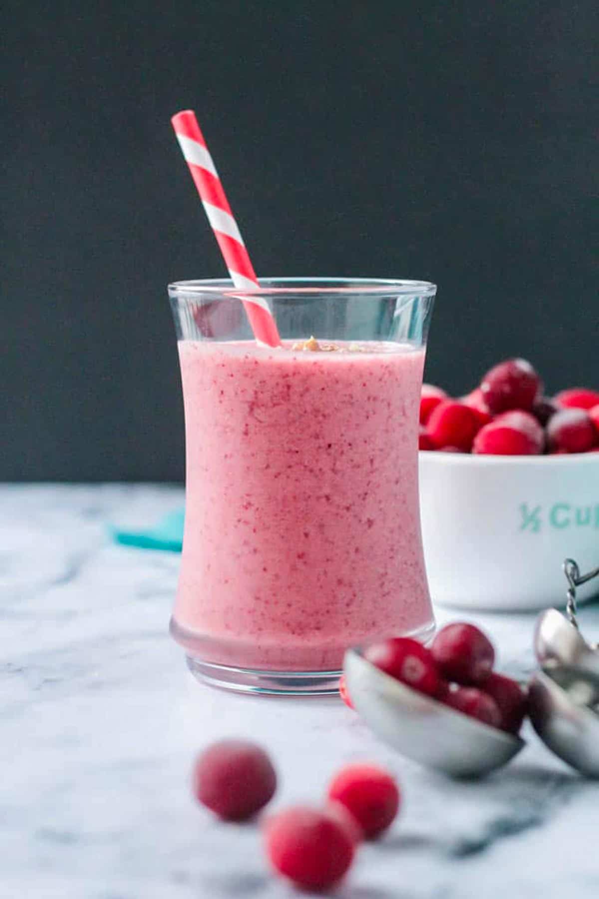 Vibrant red speckled cranberry smoothie in a glass with a red and white straw.