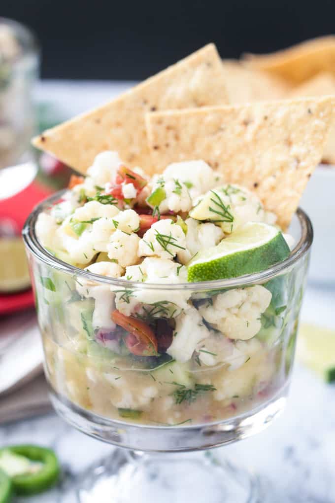 Two tortilla chips stick up from a glass bowl of cauliflower vegan ceviche.