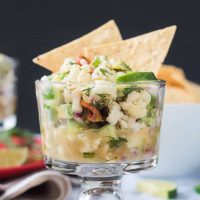 Glass bowl of cauliflower ceviche with two tortilla chips sticking out of the top.