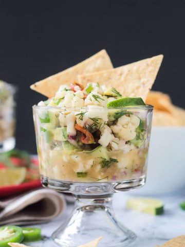 Glass bowl of cauliflower ceviche with two tortilla chips sticking out of the top.