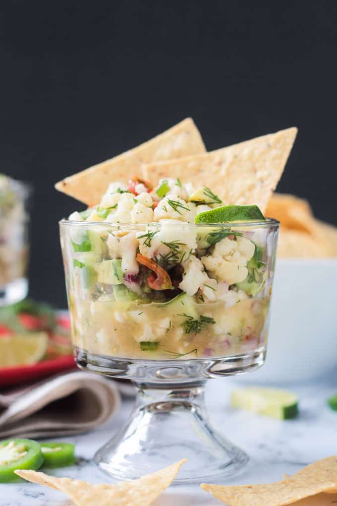 Glass bowl of cauliflower ceviche with two tortilla chips sticking out of the top.