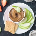 Bowl of healthy cookie butter on a plate with sliced apples and graham crackers.